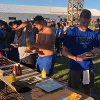 a line of football players waiting to be served food by the alumni